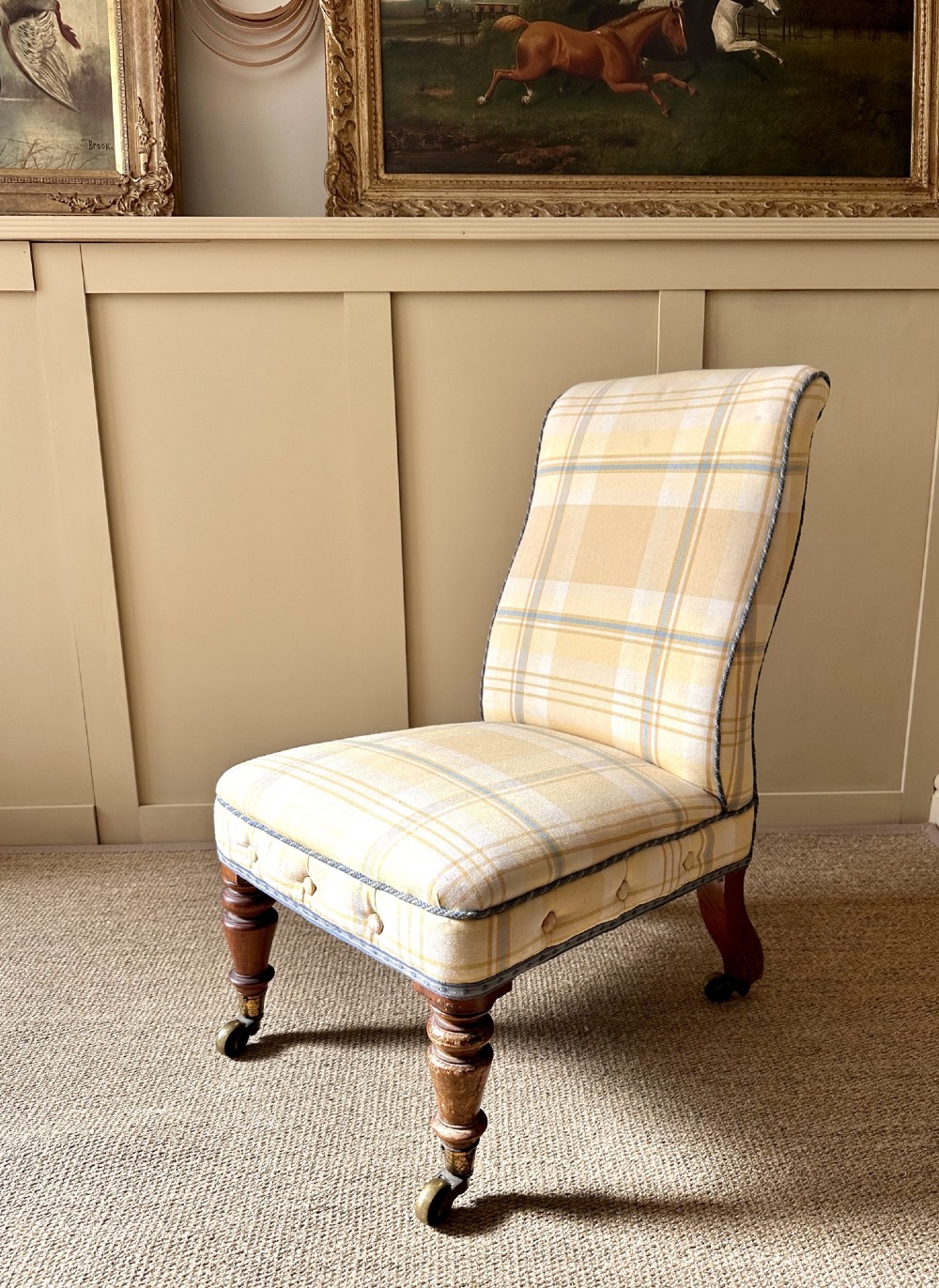 A low-seated Victorian armless slipper chair upholstered in yellow and cream tartan fabric with turned mahogany front legs on brass castors.