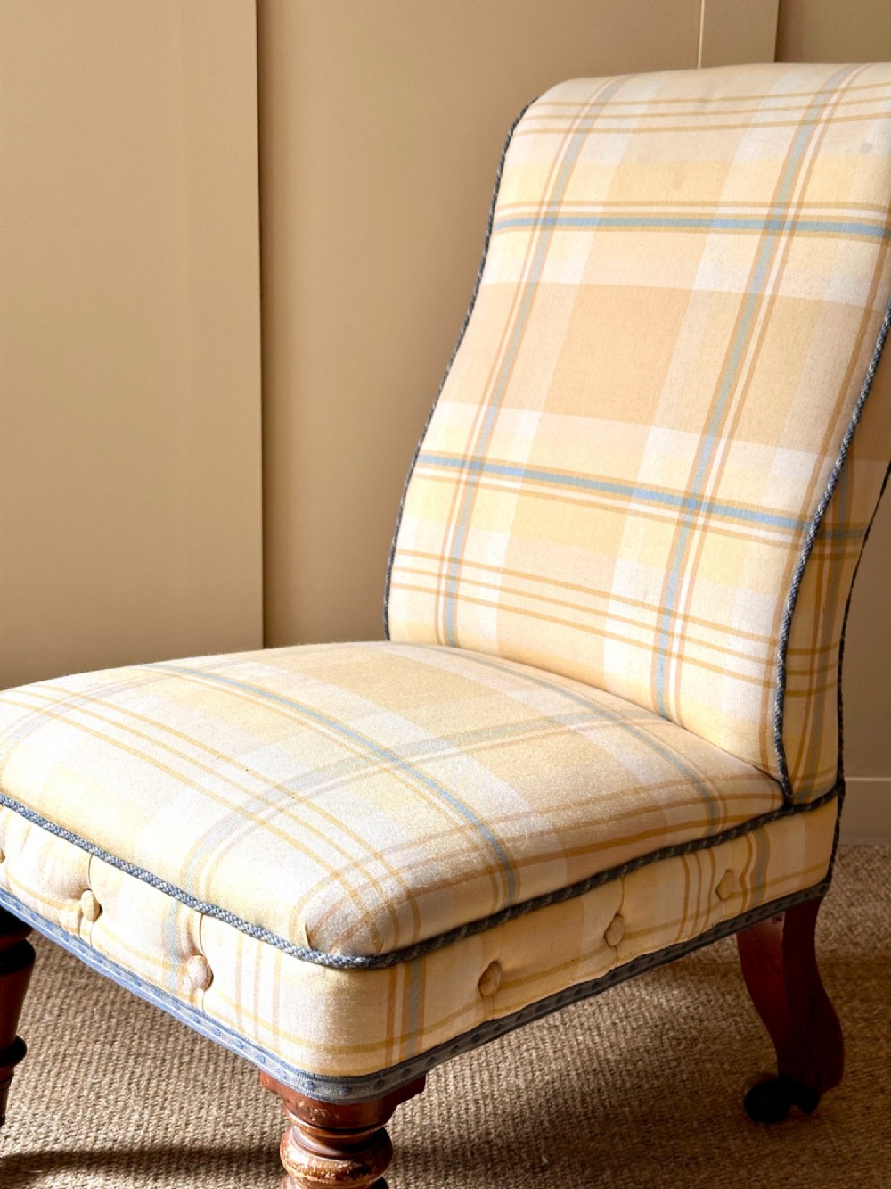 A low-seated Victorian armless slipper chair upholstered in yellow and cream tartan fabric with turned mahogany front legs on brass castors. View V