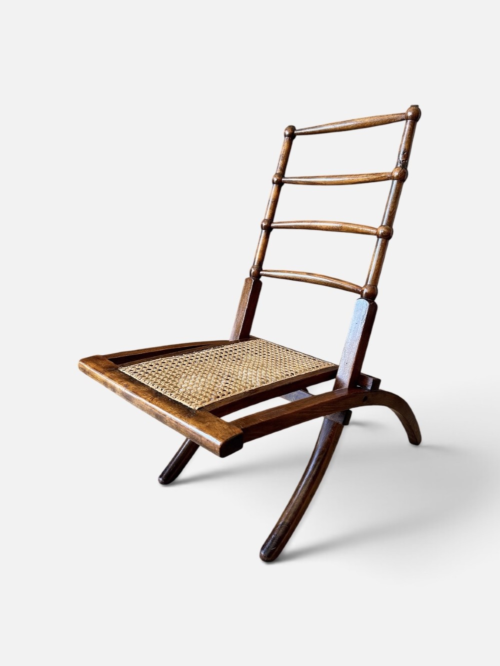 A nineteenth-century Aesthetic Movement folding campaign chair made from warm brown wood with a ladder back and woven cane seat. View II
