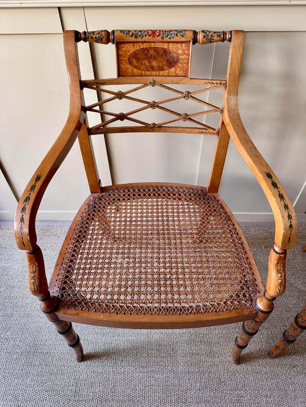 A pair of Edwardian Sheraton Revival painted wooden elbow chairs featuring woven cane seats, lattice backrests, and floral painted decoration. View III
