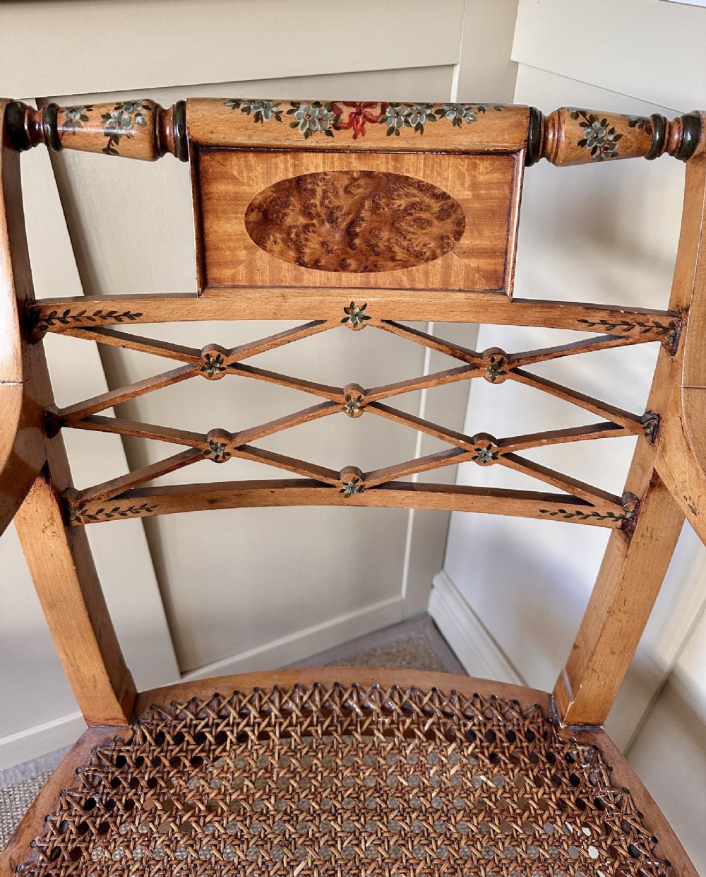 A pair of Edwardian Sheraton Revival painted wooden elbow chairs featuring woven cane seats, lattice backrests, and floral painted decoration. View IV