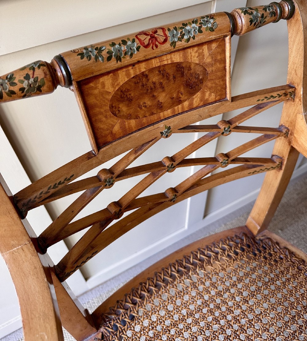 A pair of Edwardian Sheraton Revival painted wooden elbow chairs featuring woven cane seats, lattice backrests, and floral painted decoration. View V