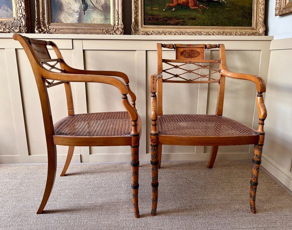 A pair of Edwardian Sheraton Revival painted wooden elbow chairs featuring woven cane seats, lattice backrests, and floral painted decoration. View VI