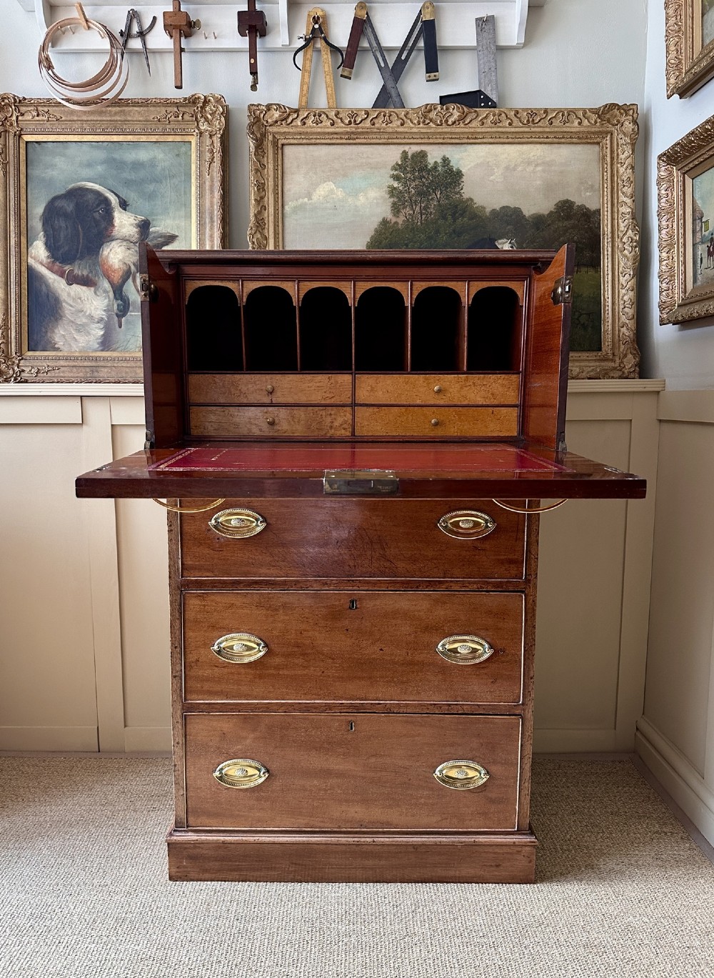 An antique nineteenth-century mahogany Wellington secretaire chest with an open drop-front writing desk section revealing internal pigeonholes above three lower drawers.