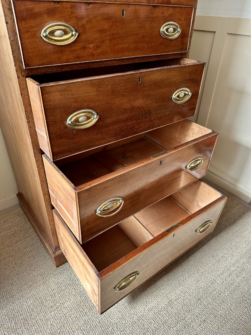 An antique nineteenth-century mahogany Wellington secretaire chest with an open drop-front writing desk section revealing internal pigeonholes above three lower drawers. View IV