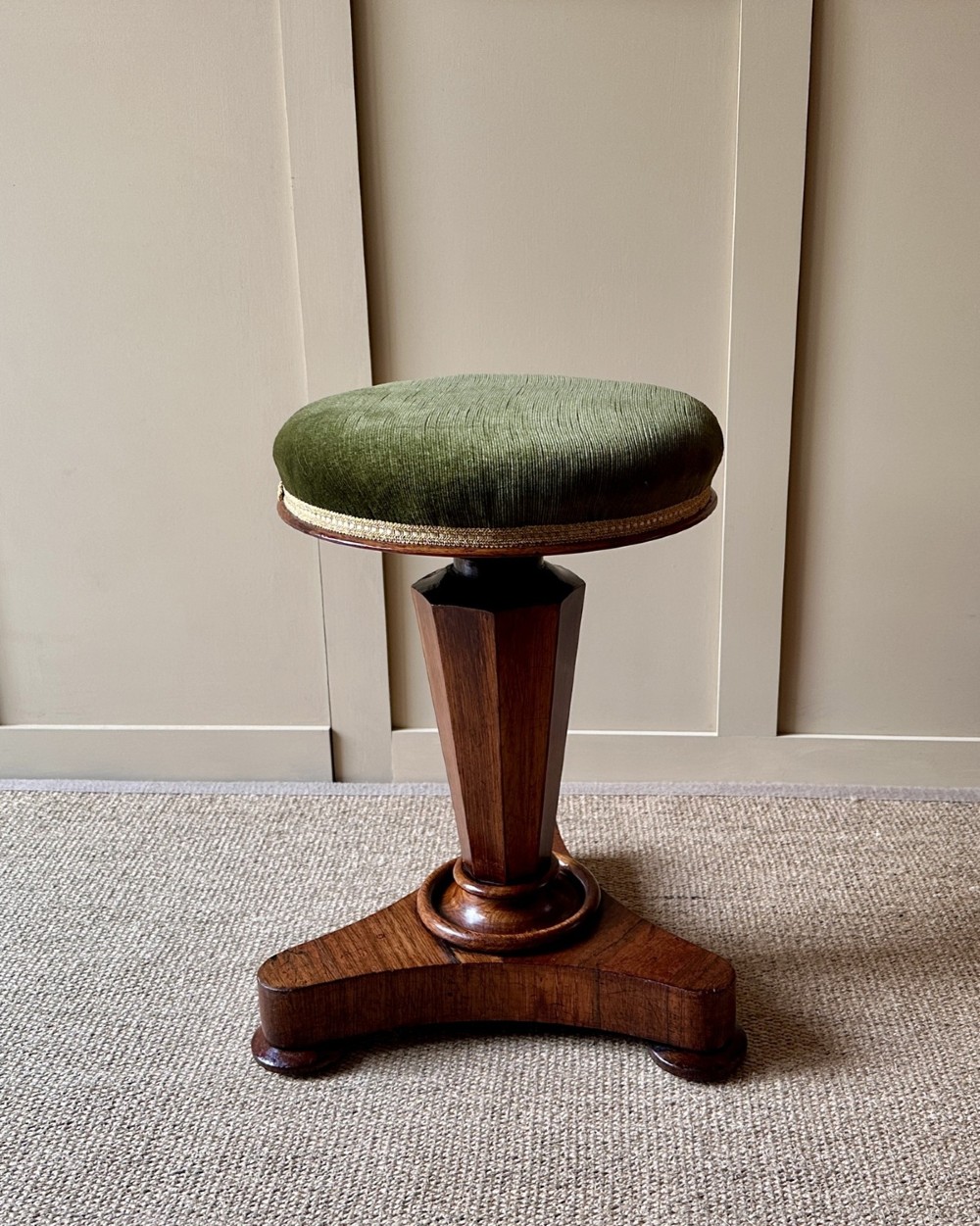 A William IV mahogany adjustable piano stool with a circular green velvet upholstered seat, supported by a faceted tapered column on a triform base.