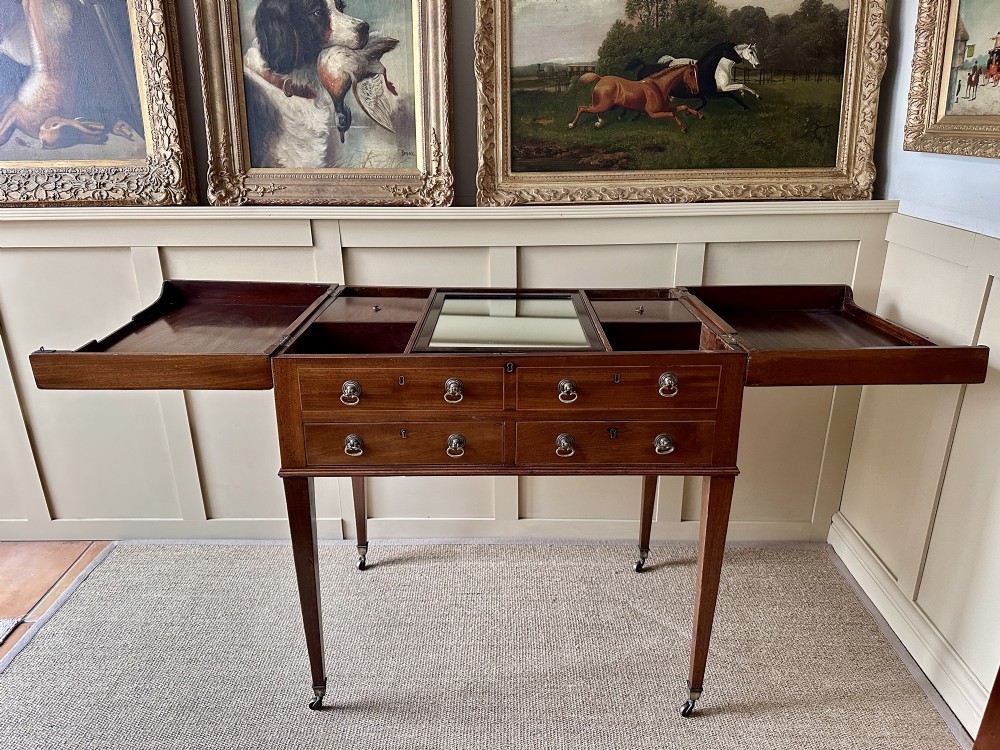 A late Georgian mahogany gentlemans dressing table featuring two hinged side leaves open to reveal internal compartments and a central adjustable mirror, raised on square tapered legs with brass castors.