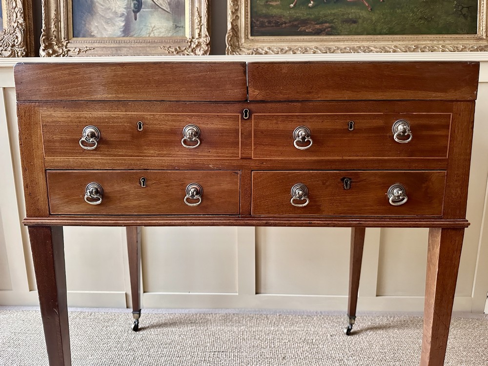 A late Georgian mahogany gentlemans dressing table featuring two hinged side leaves open to reveal internal compartments and a central adjustable mirror, raised on square tapered legs with brass castors. View II