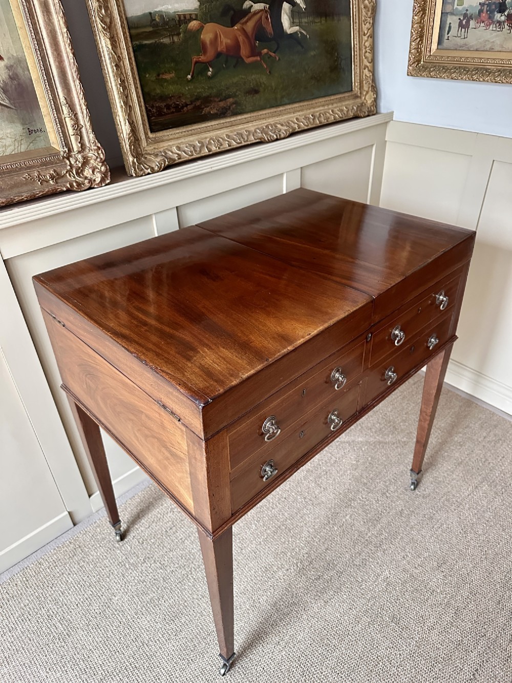 A late Georgian mahogany gentlemans dressing table featuring two hinged side leaves open to reveal internal compartments and a central adjustable mirror, raised on square tapered legs with brass castors. View V