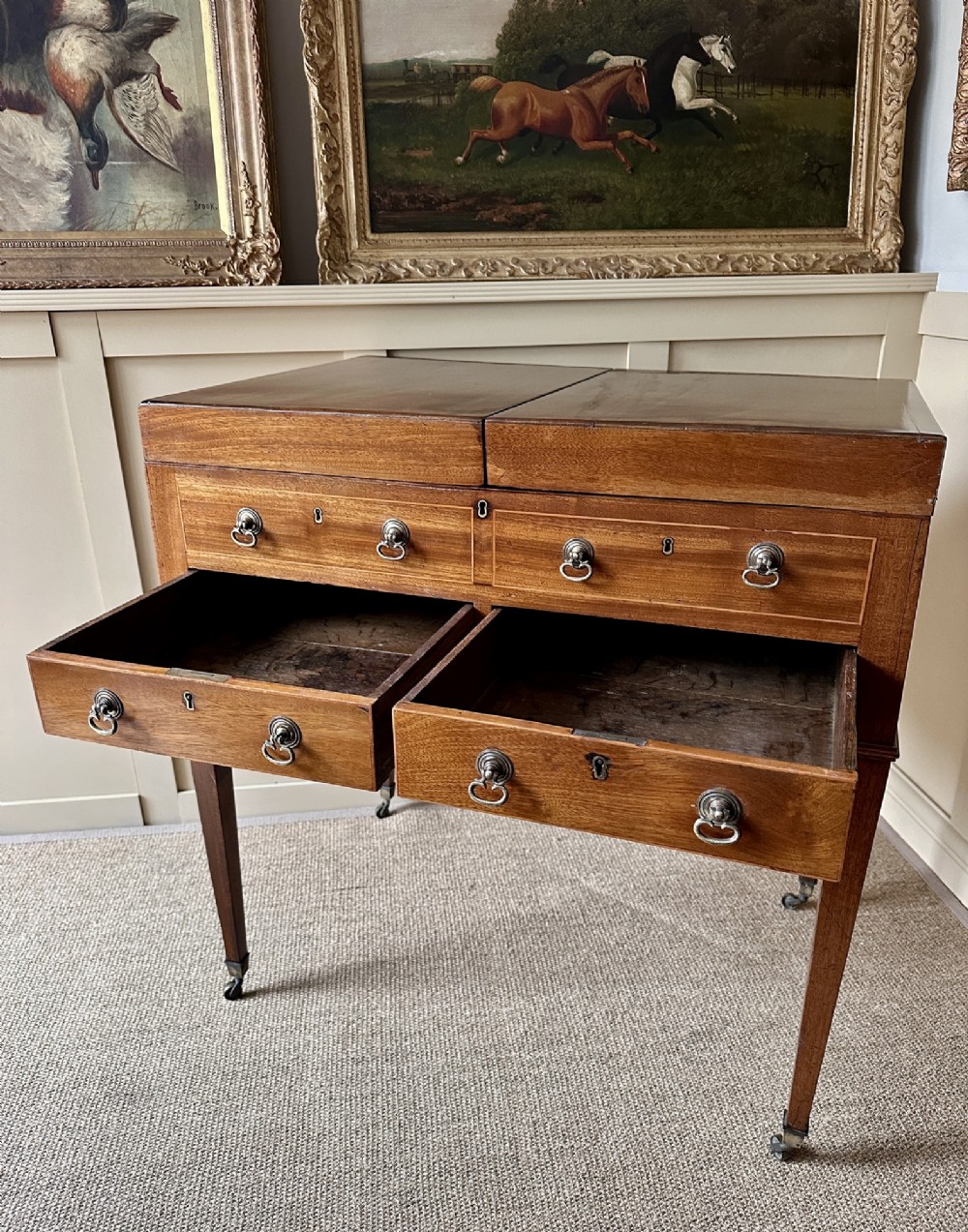A late Georgian mahogany gentlemans dressing table featuring two hinged side leaves open to reveal internal compartments and a central adjustable mirror, raised on square tapered legs with brass castors. View VI