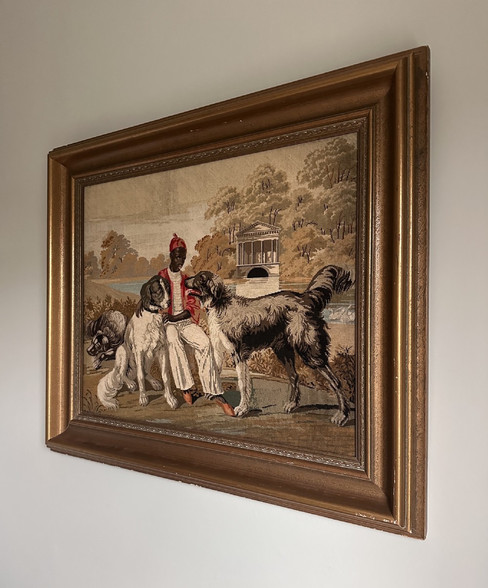 A framed Victorian Berlin woolwork tapestry depicting a seated figure with two dogs in a parkland setting within a moulded gilt frame. View V