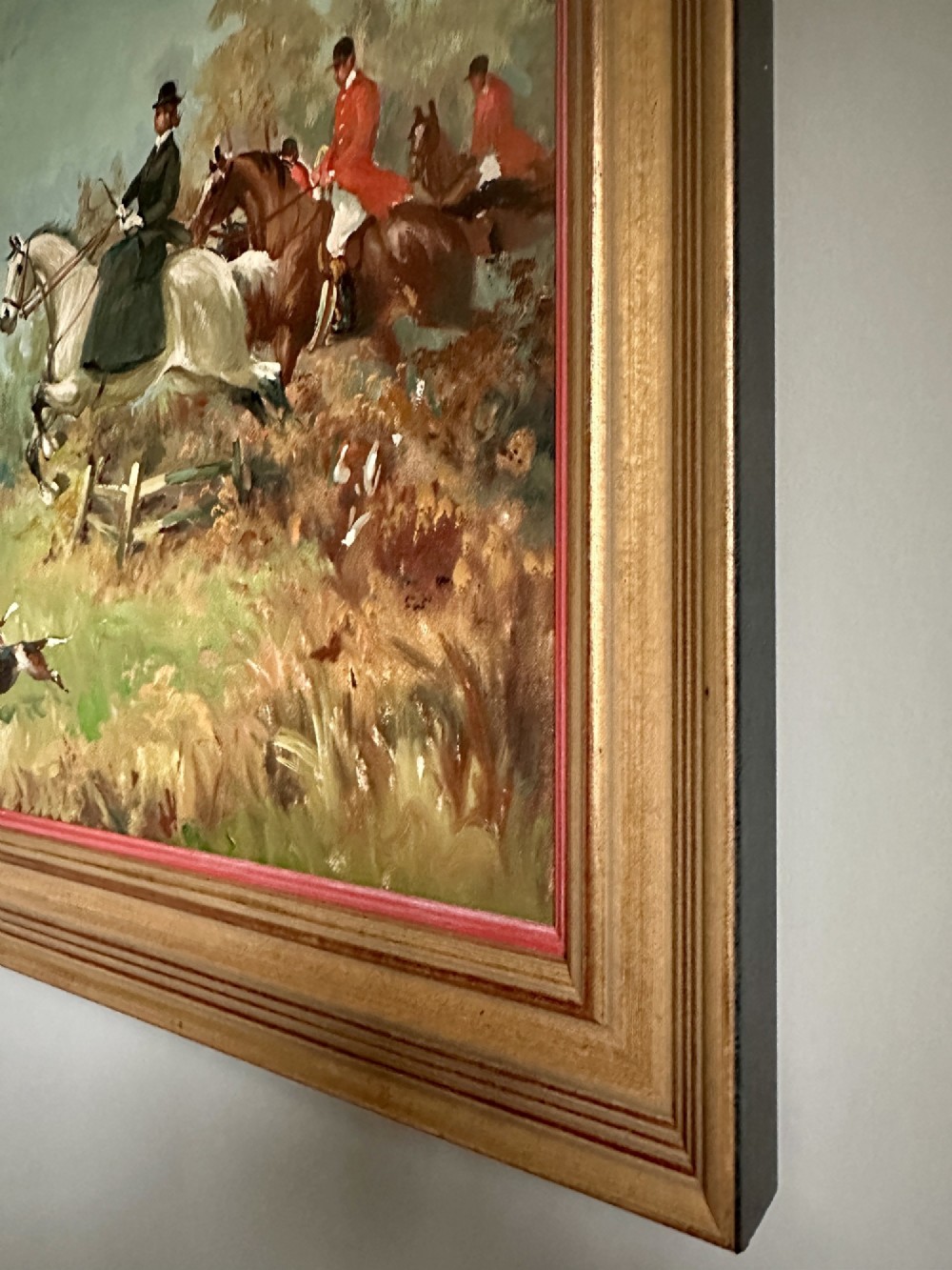 An oil painting depicting a fox hunting scene with horse riders and foxhounds across a green countryside landscape, presented in a gold gilded wooden frame. View VI