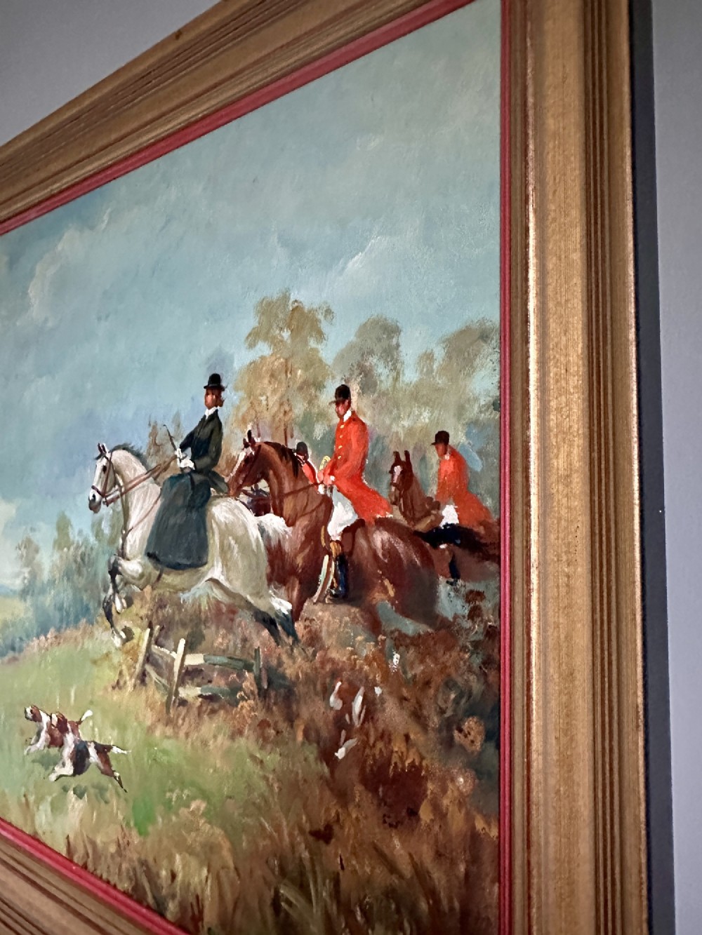 An oil painting depicting a fox hunting scene with horse riders and foxhounds across a green countryside landscape, presented in a gold gilded wooden frame. View VII