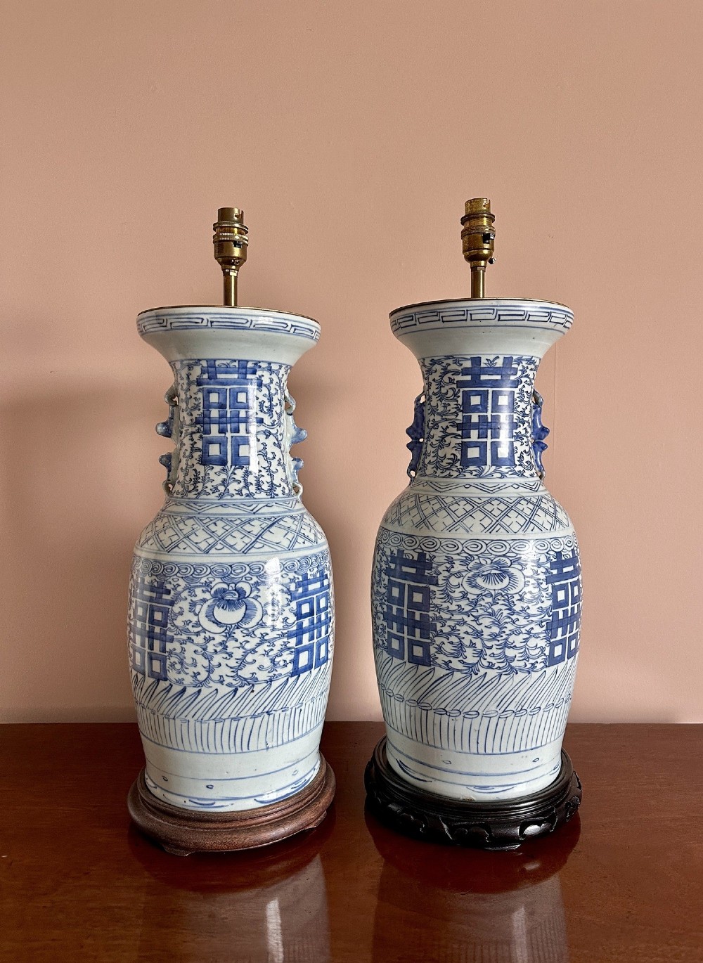 A pair of baluster-shaped blue and white Chinese porcelain table lamps featuring hand-painted Double Happiness symbols and floral scrolls set on dark carved wooden bases.