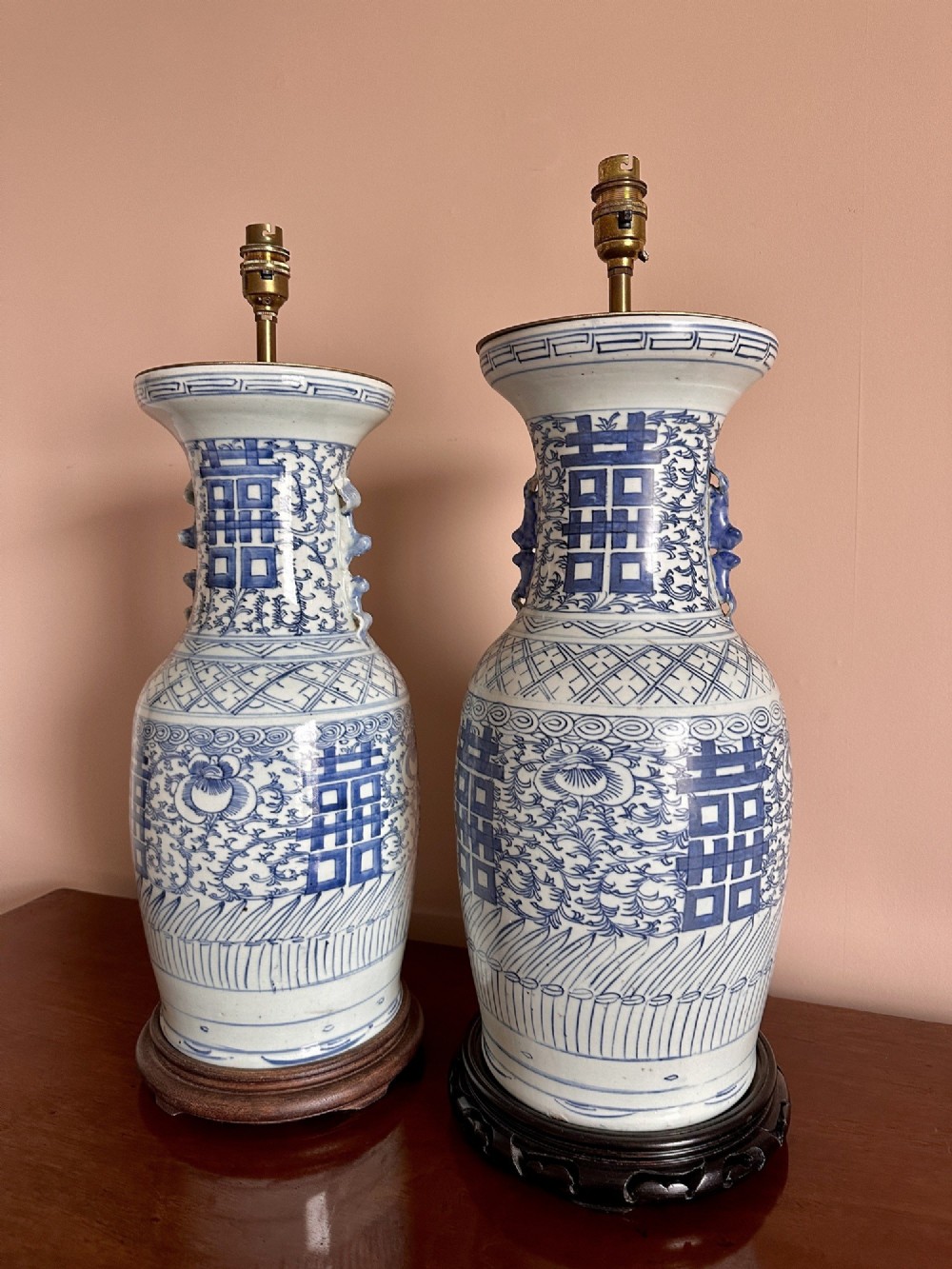 A pair of baluster-shaped blue and white Chinese porcelain table lamps featuring hand-painted Double Happiness symbols and floral scrolls set on dark carved wooden bases. View II
