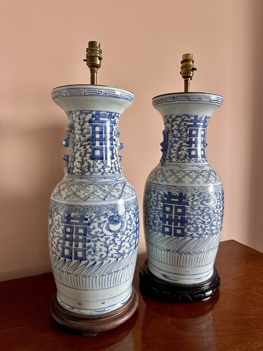 A pair of baluster-shaped blue and white Chinese porcelain table lamps featuring hand-painted Double Happiness symbols and floral scrolls set on dark carved wooden bases. View III