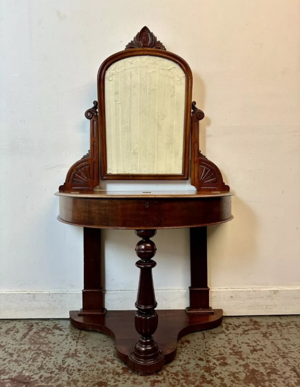A late 19th-century Victorian mahogany Duchess dressing table with an arched mirror frame, carved cresting, turned central leg, and shaped plinth base.