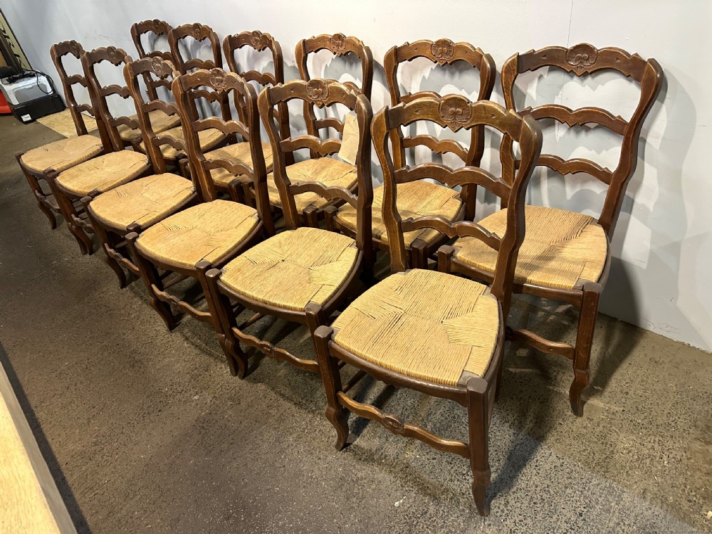 A set of twelve French provincial ladder back dining chairs featuring woven rush seats and carved timber frames.