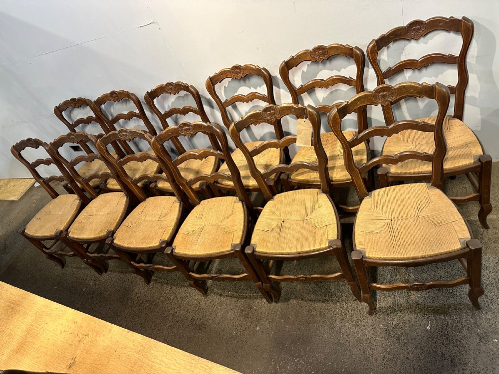 A set of twelve French provincial ladder back dining chairs featuring woven rush seats and carved timber frames. View VI