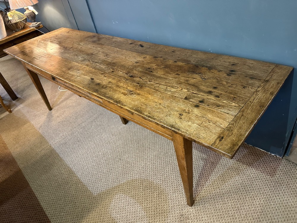 A long 19th-century oak table featuring a plank top, three front drawers with metal ring pulls, and four tapered square legs. View II