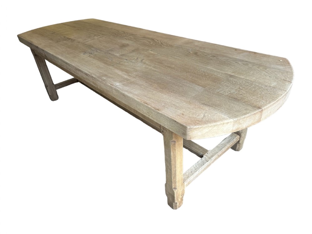 An overhead view of a long, bleached oak refectory table with rounded oval ends and sturdy stretcher-base legs.
