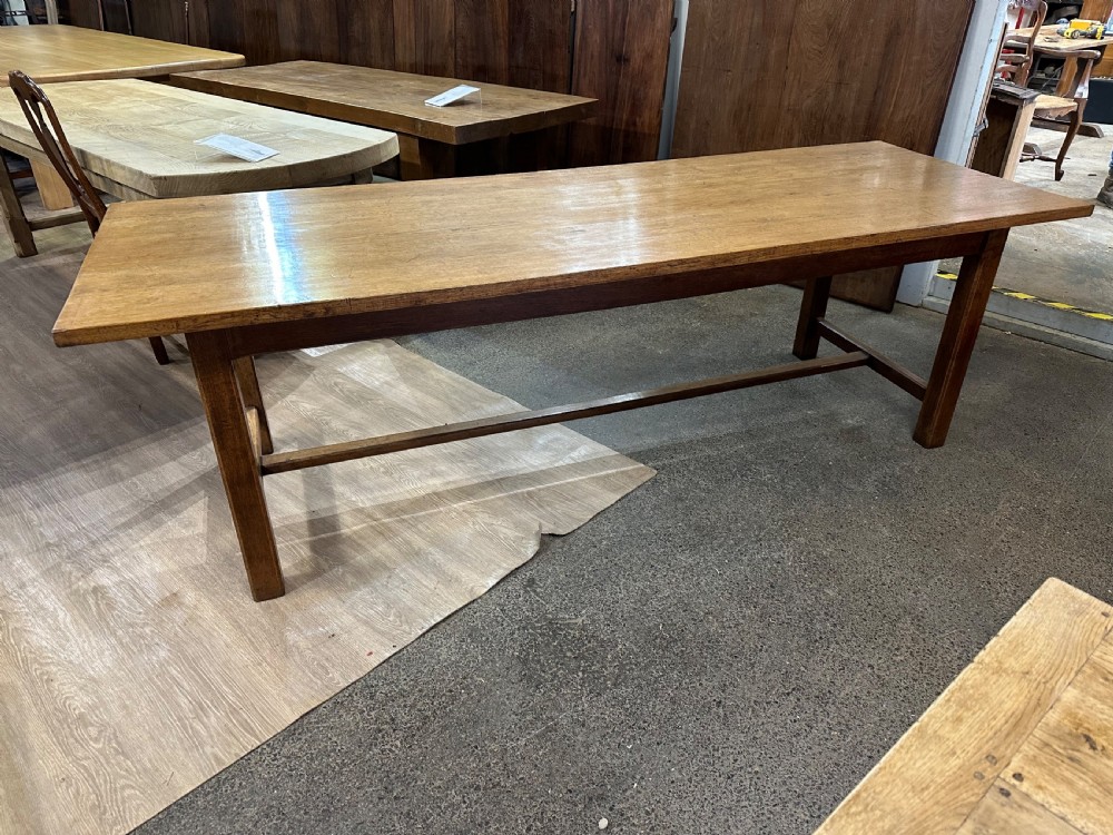 A long rectangular antique oak farmhouse dining table featuring a plank top and an H-stretcher base structure. View IV