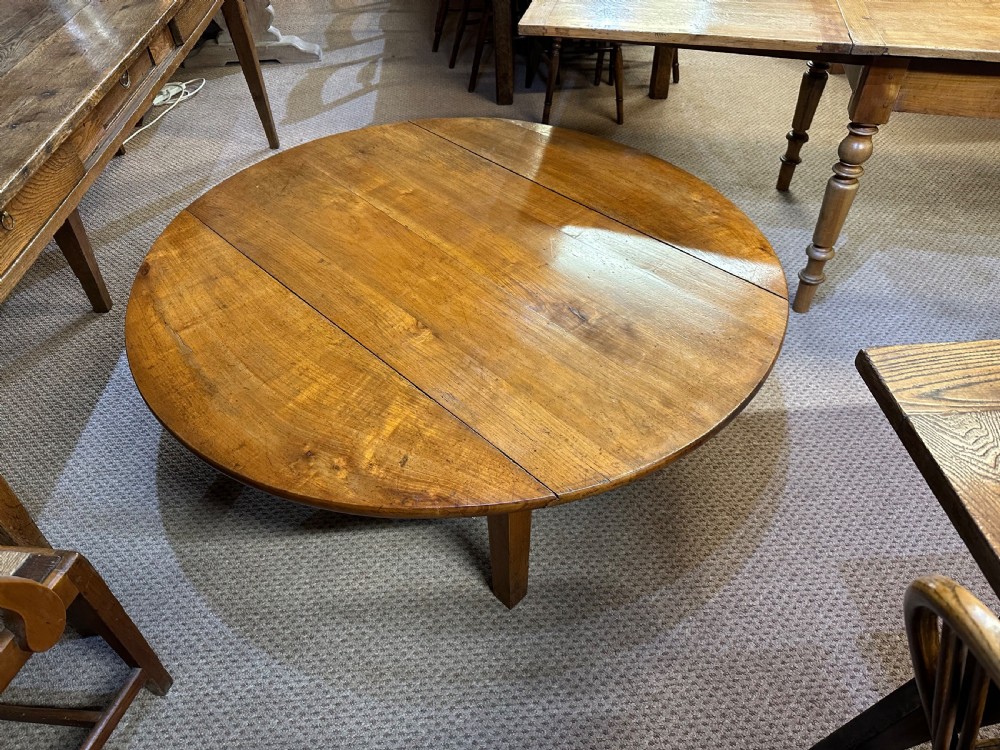 A nineteenth-century round cherrywood coffee table featuring two drop-leaf side flaps and straight wooden legs. View II