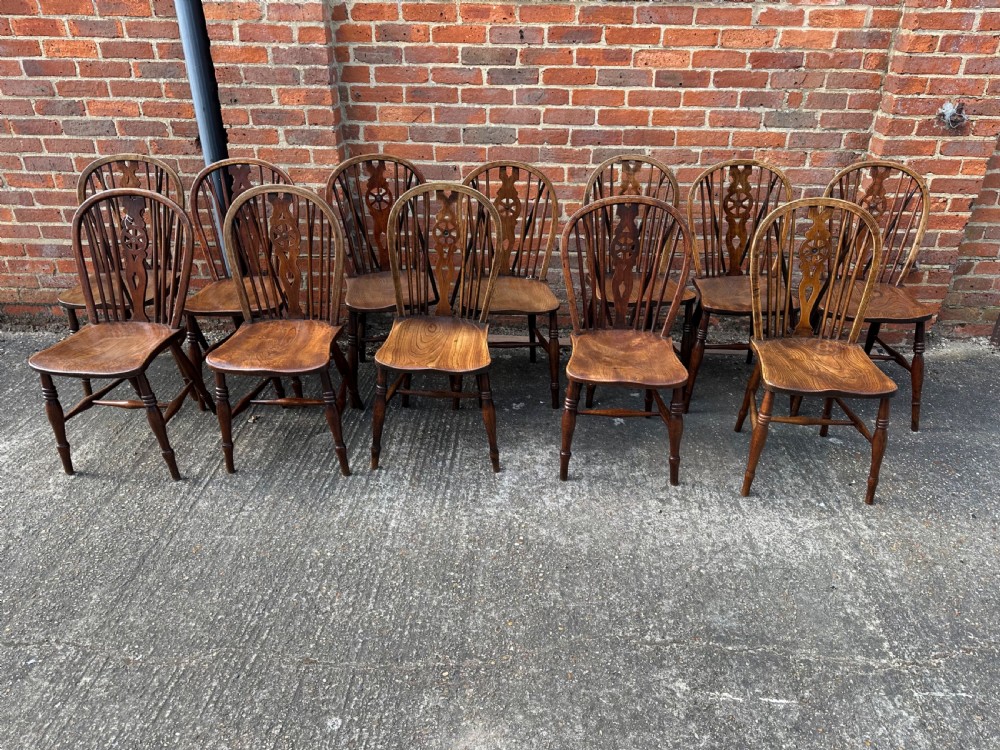 A set of twelve antique wooden Windsor dining chairs with hoop backs, pierced wheelback splats, contoured saddled seats, and turned legs with stretcher bases. View II