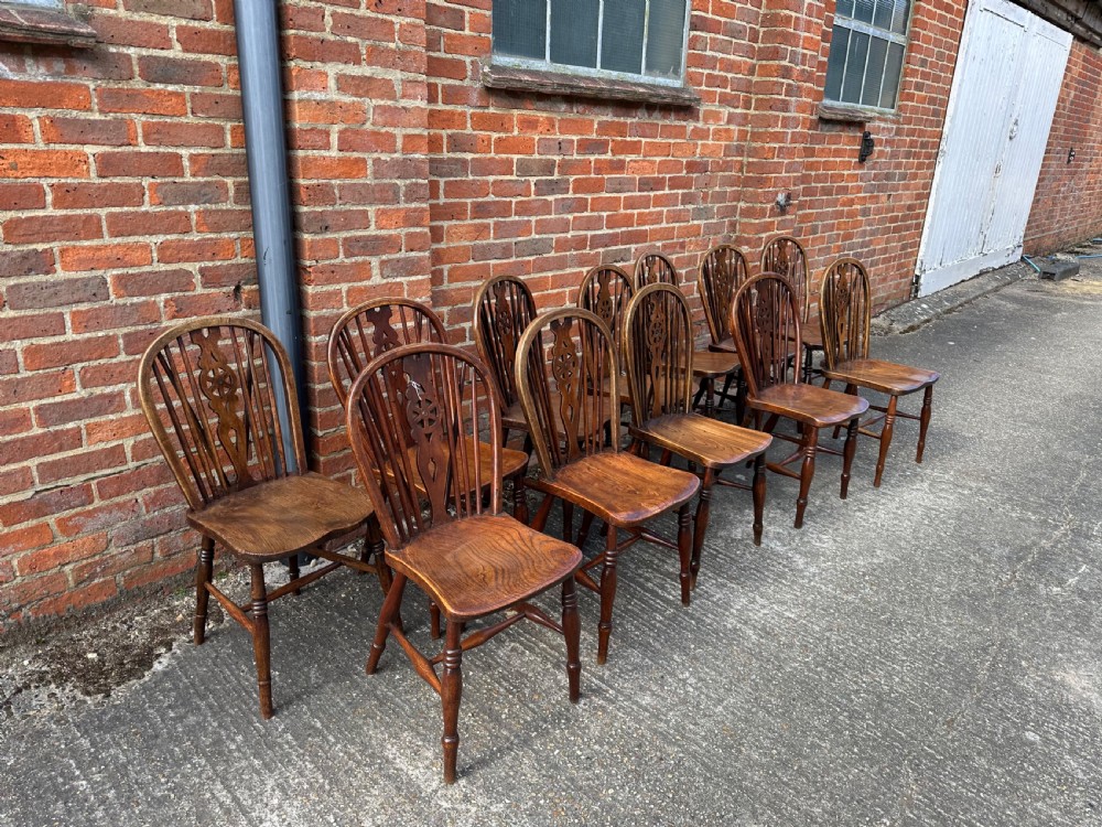 A set of twelve antique wooden Windsor dining chairs with hoop backs, pierced wheelback splats, contoured saddled seats, and turned legs with stretcher bases. View V