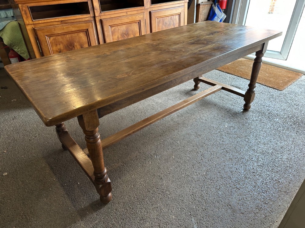A long rectangular antique elm dining table featuring turned wooden legs connected by a central stretcher base and a smooth timber top. View II