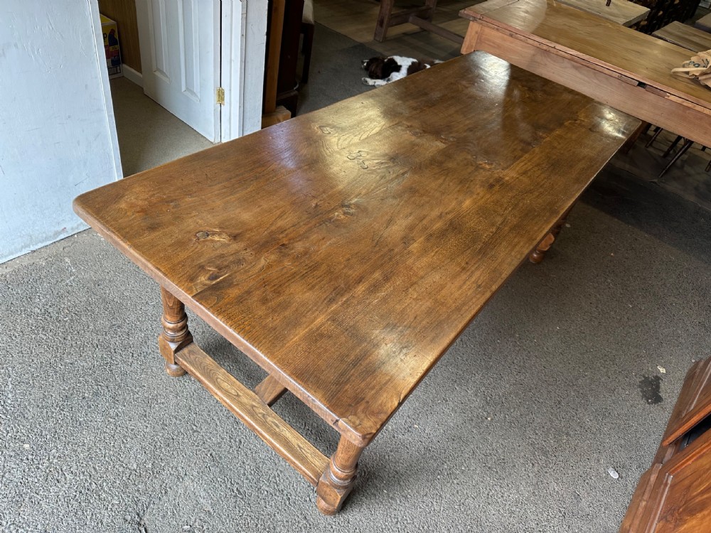 A long rectangular antique elm dining table featuring turned wooden legs connected by a central stretcher base and a smooth timber top. View III