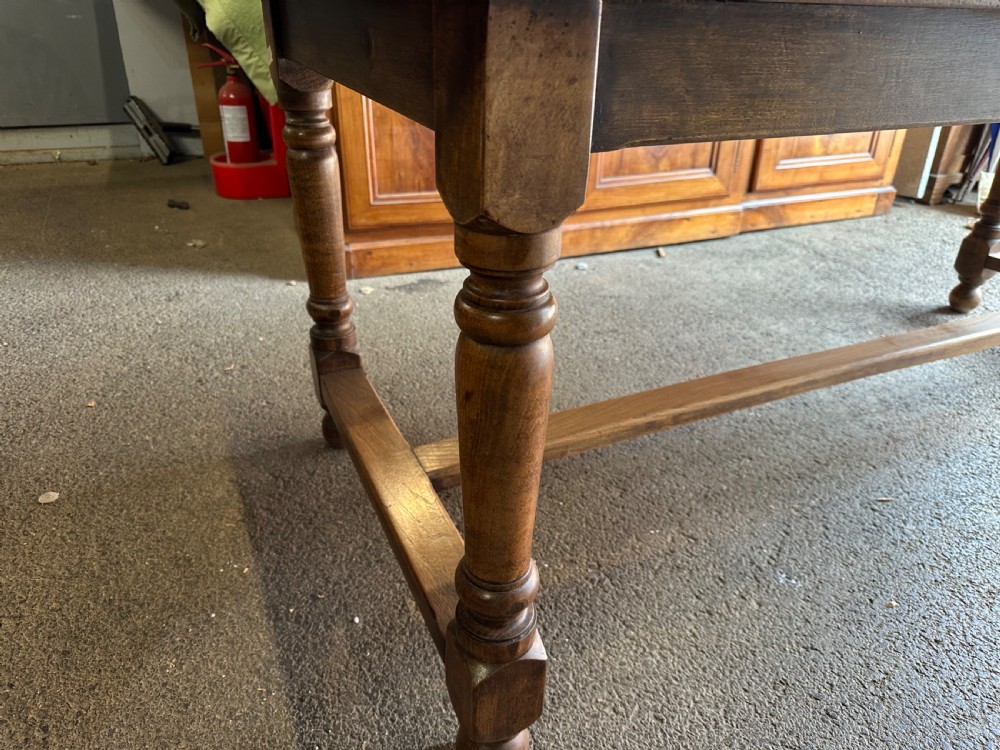 A long rectangular antique elm dining table featuring turned wooden legs connected by a central stretcher base and a smooth timber top. View V