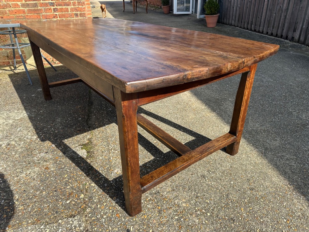 An early nineteenth-century solid walnut dining table featuring a wide plank top with natural patina and square legs linked by low stretchers. View IV