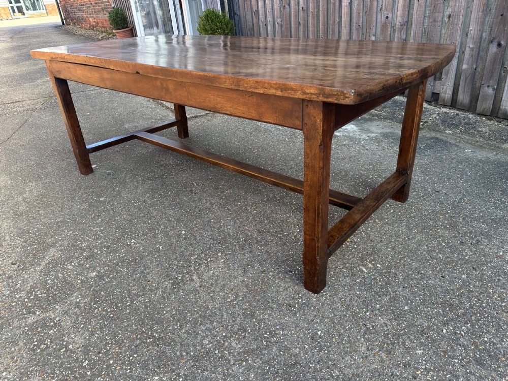 An early nineteenth-century solid walnut dining table featuring a wide plank top with natural patina and square legs linked by low stretchers. View V