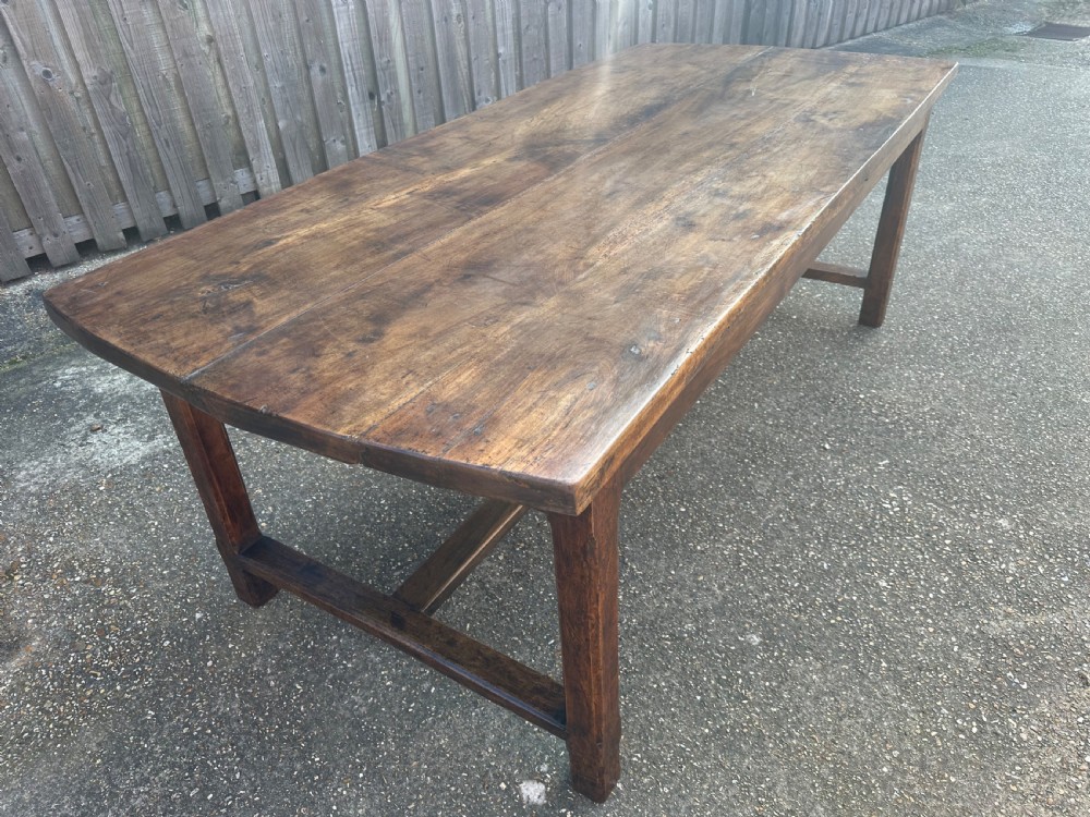 An early nineteenth-century solid walnut dining table featuring a wide plank top with natural patina and square legs linked by low stretchers. View VI