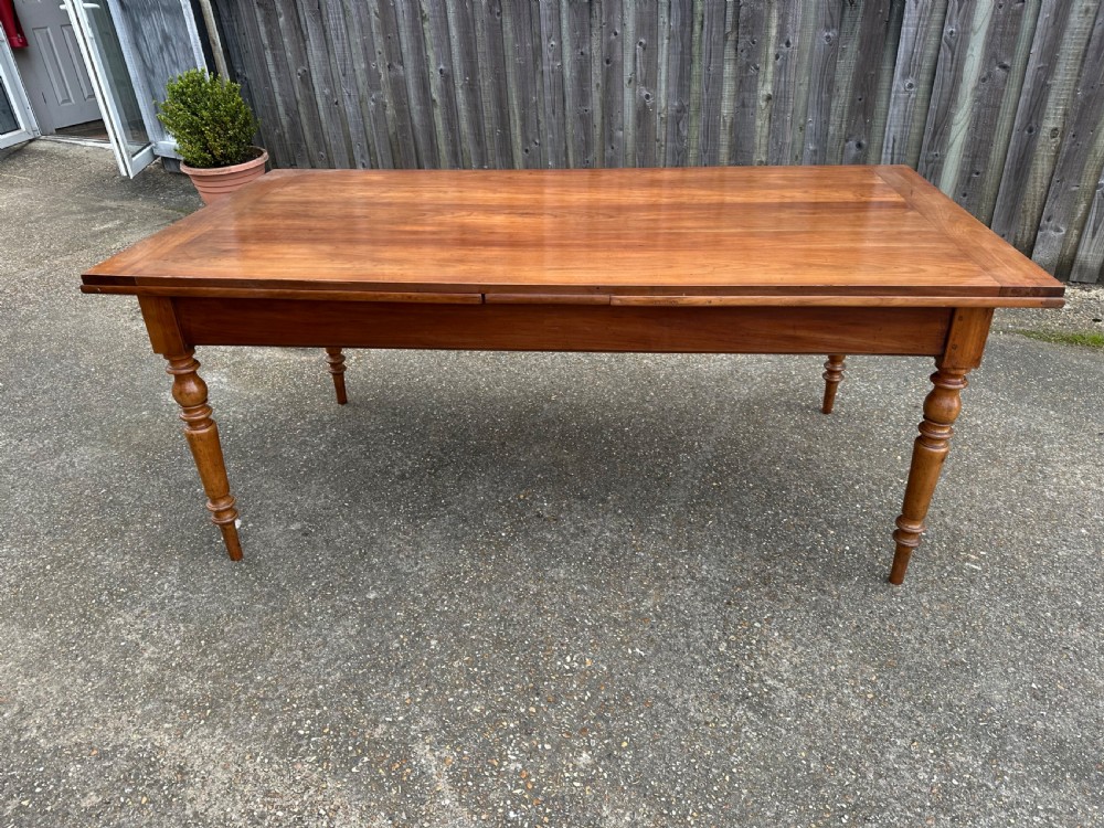 A 19th-century cherry wood extending dining table featuring turned legs and side extension leaves on a plain background. View II