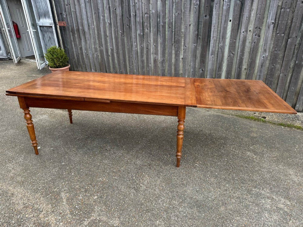 A 19th-century cherry wood extending dining table featuring turned legs and side extension leaves on a plain background. View V