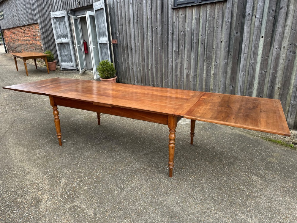 A 19th-century cherry wood extending dining table featuring turned legs and side extension leaves on a plain background. View VI