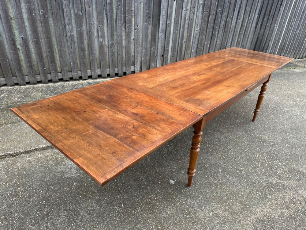 A 19th-century cherry wood extending dining table featuring turned legs and side extension leaves on a plain background. View VII