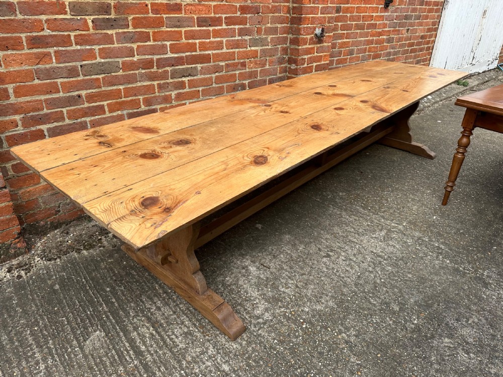 A long rectangular pine trestle dining table with a multi-plank top and a central timber stretcher base. View III
