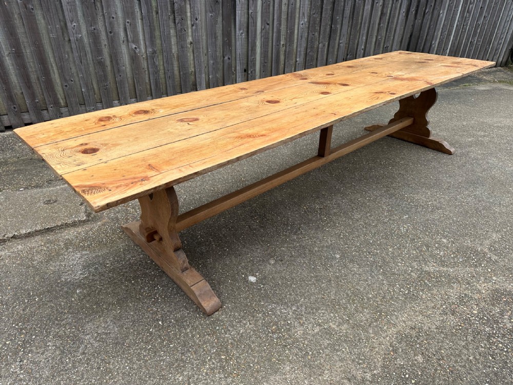 A long rectangular pine trestle dining table with a multi-plank top and a central timber stretcher base. View V