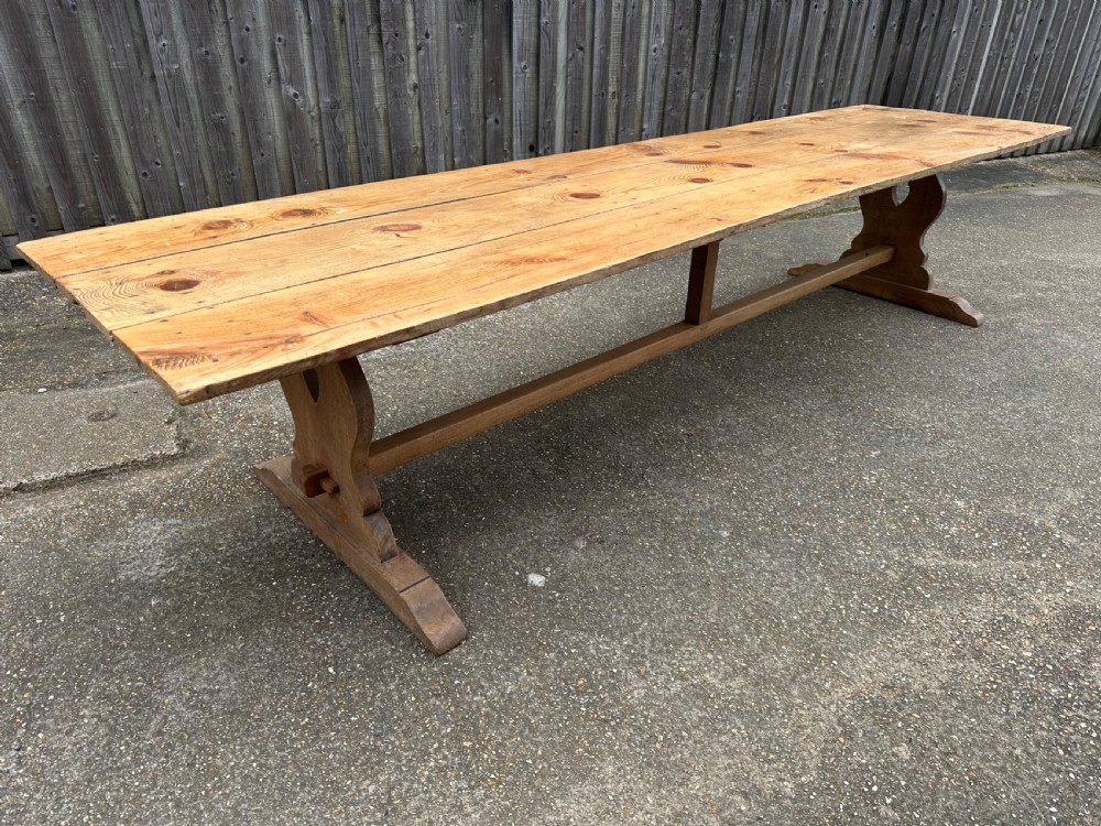 A long rectangular pine trestle dining table with a multi-plank top and a central timber stretcher base. View VI