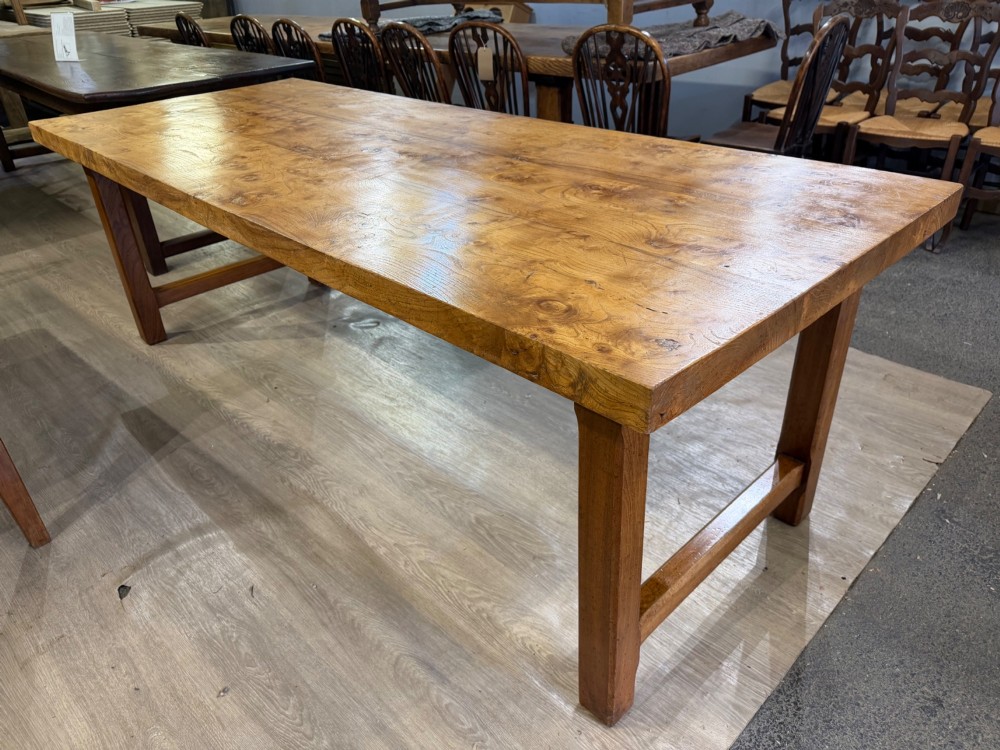 A long rectangular wooden farmhouse dining table featuring a plank top and sturdy trestle leg base in a warm honey oak finish. View II