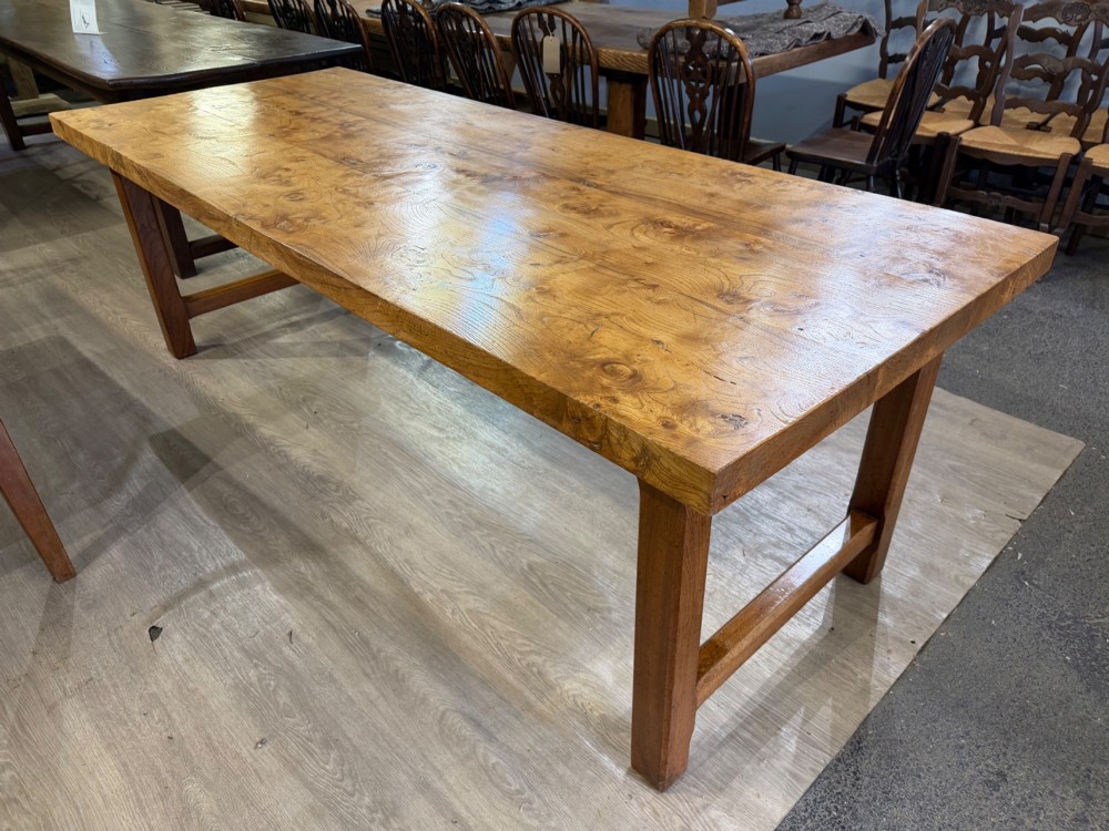 A long rectangular wooden farmhouse dining table featuring a plank top and sturdy trestle leg base in a warm honey oak finish. View III