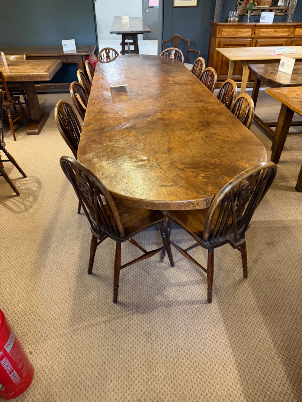 A long antique oak dining table featuring a thick single plank top with rounded ends supported by a low wooden stretcher base. View II