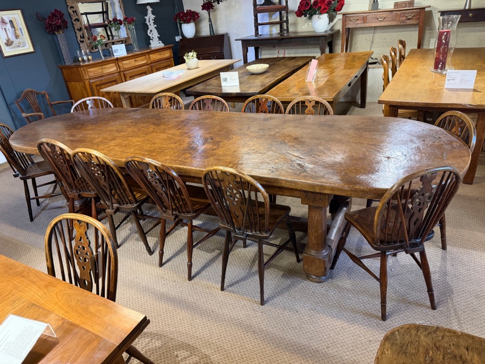 A long antique oak dining table featuring a thick single plank top with rounded ends supported by a low wooden stretcher base. View III