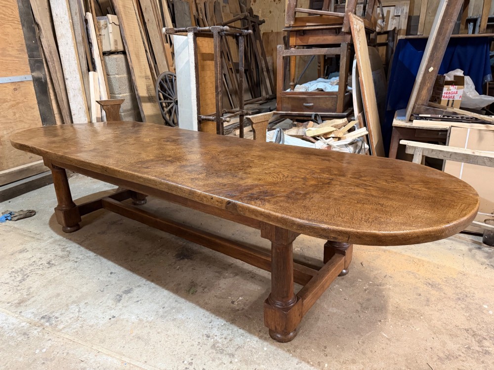 A long antique oak dining table featuring a thick single plank top with rounded ends supported by a low wooden stretcher base. View V