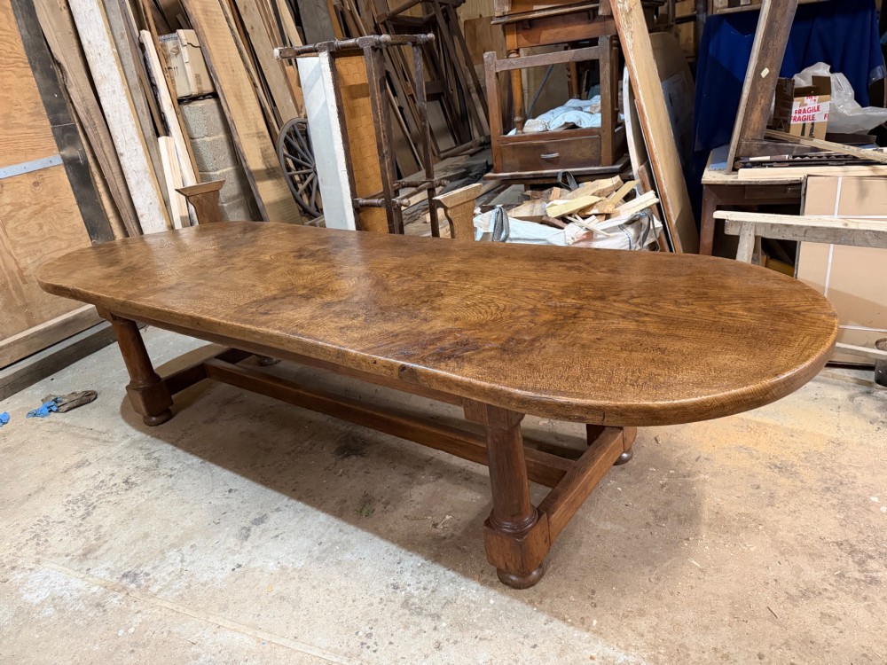 A long antique oak dining table featuring a thick single plank top with rounded ends supported by a low wooden stretcher base. View VI