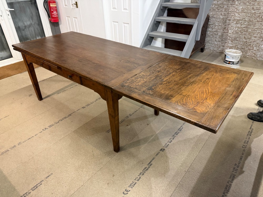 A long antique oak extending dining table featuring two end extension leaves, side frieze drawers, and tapered square legs. View VIII