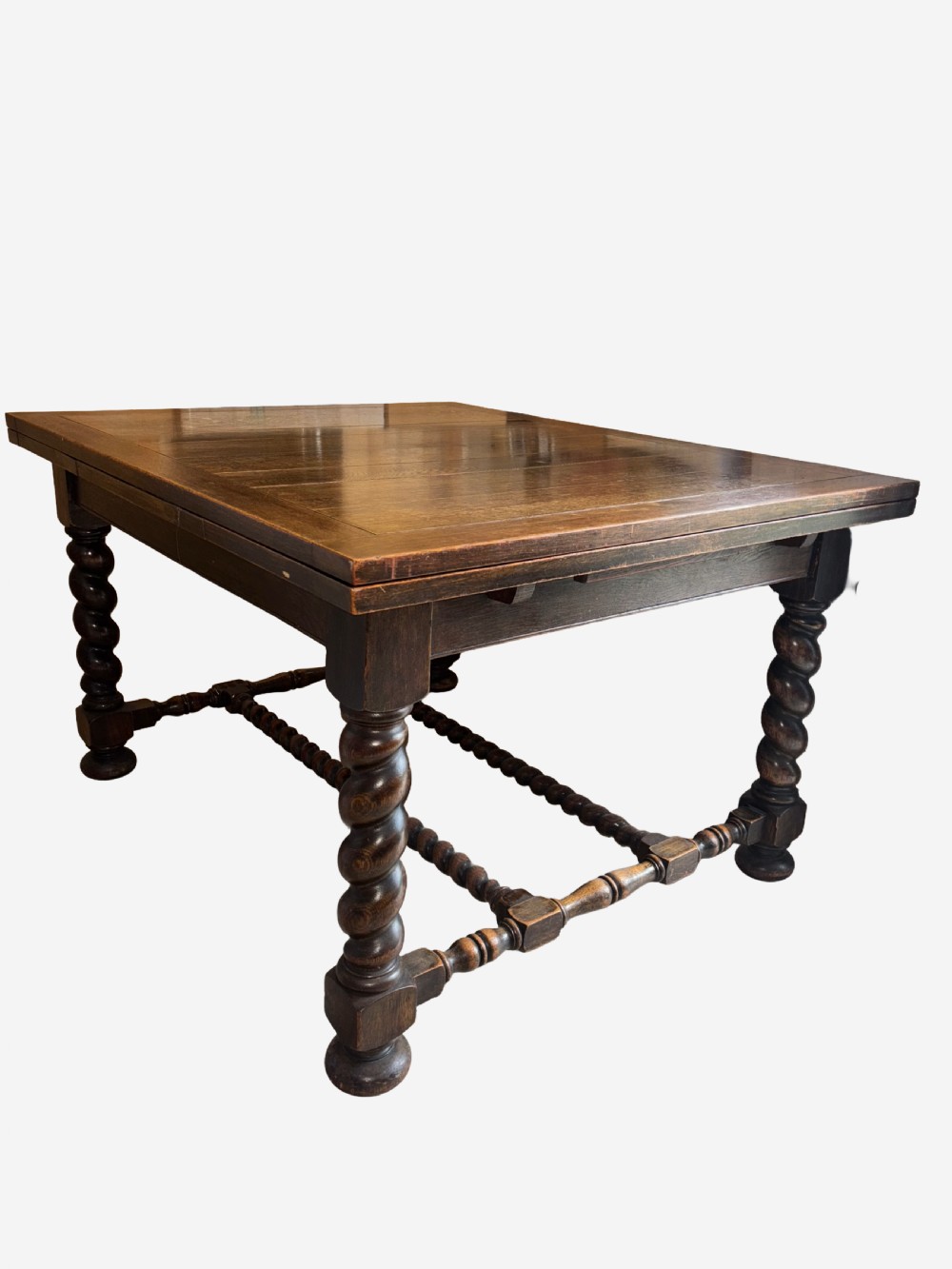 A dark oak draw-leaf dining table supported by four thick barley twist legs and low turned stretchers.